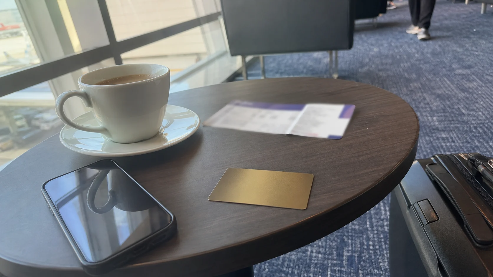 空港ラウンジで搭乗前にスマートフォンを確認している旅行者とコーヒーのイメージ